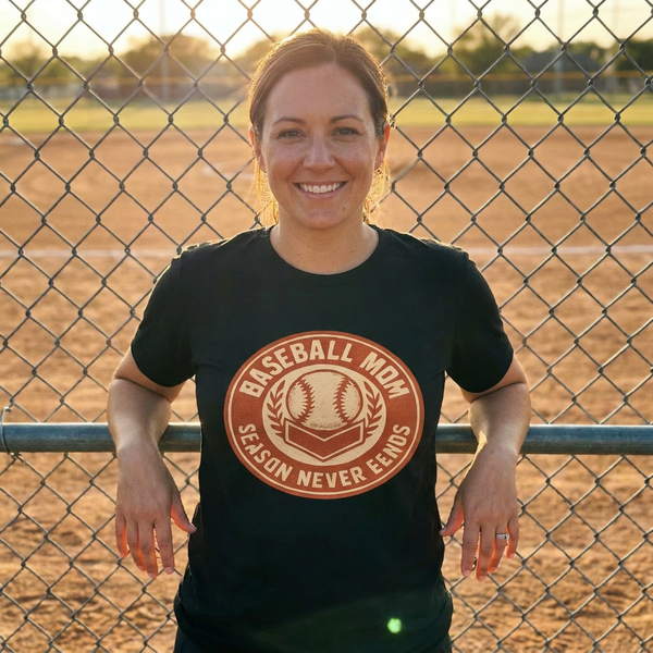Baseball mom wearing sideline crew vintage badge tee at the diamond fence, golden hour, lifestyle photo