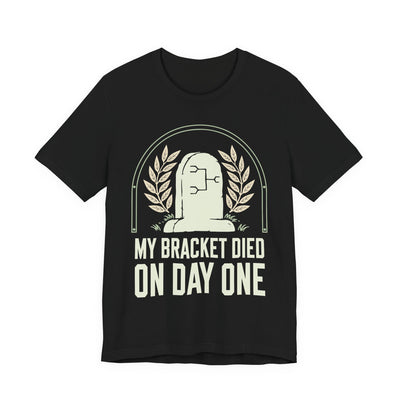 My Bracket Died On Day One tee flat front, black unisex tee, a headstone with a bracket diagram carved on it