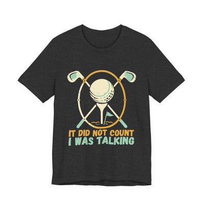 It Did Not Count I Was Talking tee flat front, dark grey heather unisex tee, golf clubs behind a ball on a tee