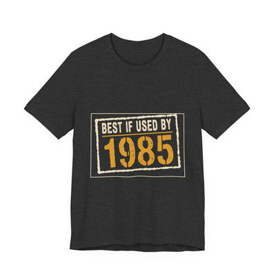 Best If Used By 1985 tee flat front, dark grey heather unisex tee, cream expiry stamp, amber year