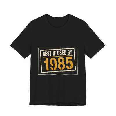 Best If Used By 1985 tee flat front, black unisex tee, cream expiry stamp, amber year