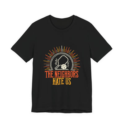 The Neighbors Hate Us tee flat front, black unisex tee, pickleball paddle sunburst badge