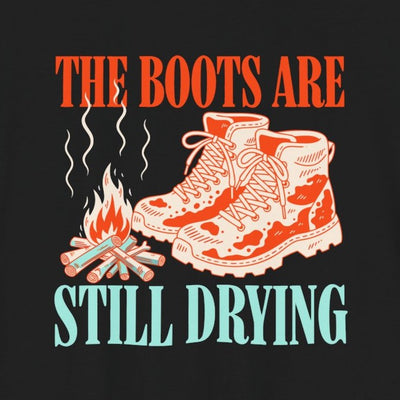 The Boots Are Still Drying tee print close-up, black unisex tee, muddy boots by a campfire