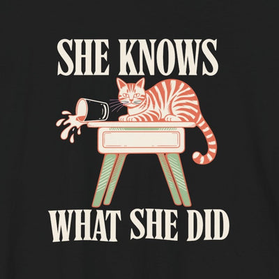 She Knows What She Did tee print close-up, black unisex tee, tabby cat by a falling glass