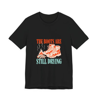 The Boots Are Still Drying tee flat front, black unisex tee, muddy boots by a campfire
