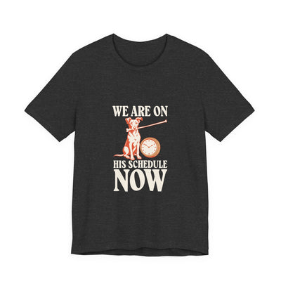 We Are On His Schedule Now tee flat front, dark grey heather unisex tee, dog beside a wall clock