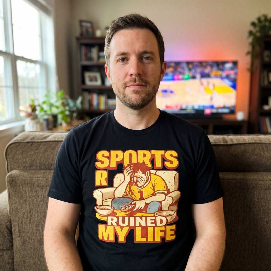 Man wearing Sports Ruined My Life black tee on couch with the game on TV, funny sports fan graphic