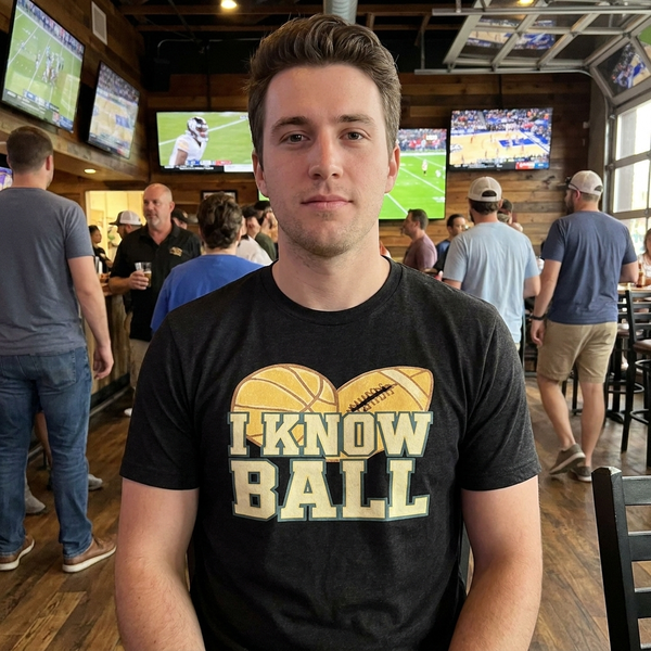 Man at a sports bar wearing a black I Know Ball t-shirt with distressed basketball and football graphic