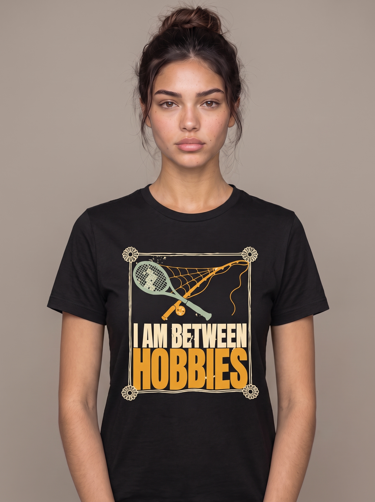 I Am Between Hobbies tee worn front view, black unisex tee, a dusty tennis racket and fishing rod crossed