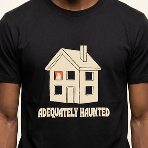 Adequately Haunted tee worn front view, black unisex tee, plain house with one ghost in an upstairs window